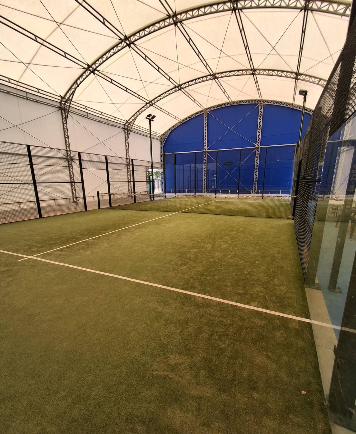 Campo da padel in erba sintetica sotto la copertura, con la parete di fondo blu